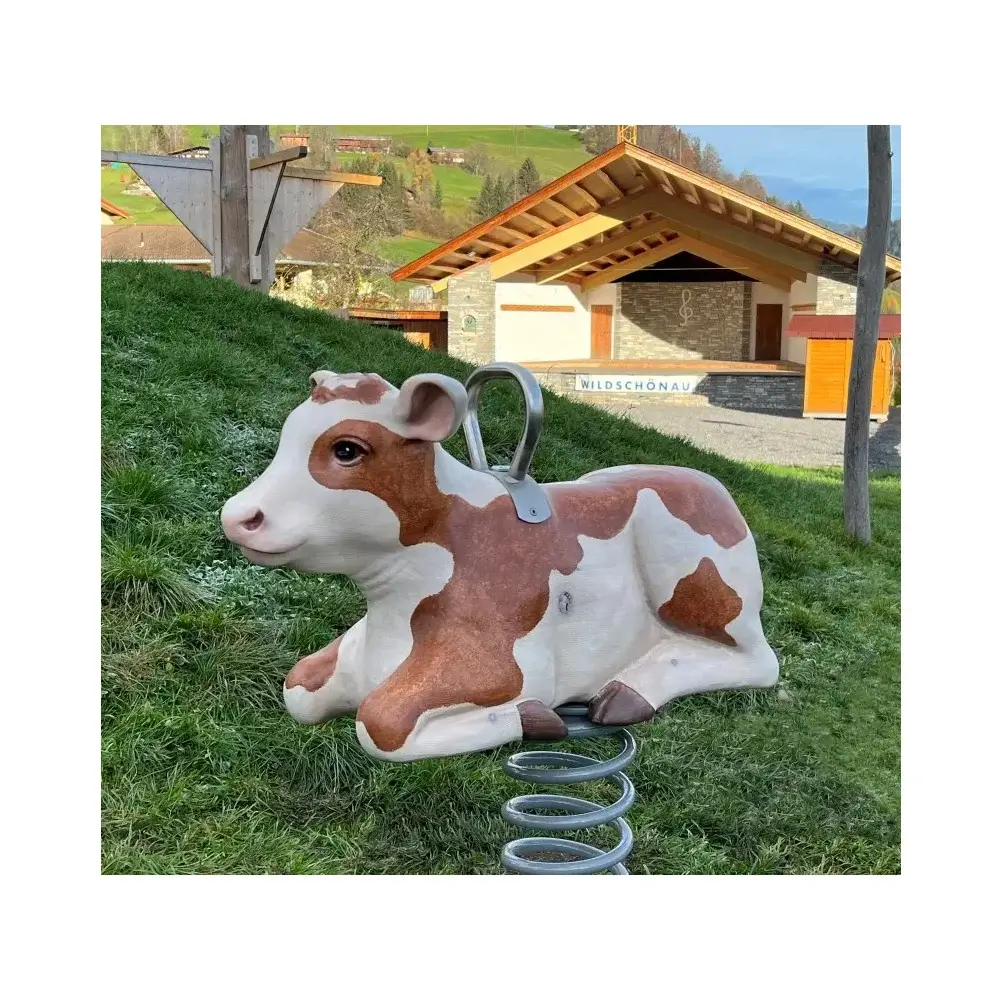 Foto: geschnitzes und bemaltes Federwipptier Kalb auf grauer Schwungfeder und mit Edelstahlhaltebügel auf dem Rücken. im Hintergrund Berglandschaft