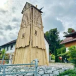 Foto von der Rückseite des Spielturm Zuckerhut: Der Robinienturm läuft von seiner quadratischen Grundform bis auf ca. 5 m Höhe mehr oder weniger spitz zusammen. die unteren Ebenen sind vollständig verschlagen. die obereste Ebene hat einen lockeren Lattenverschlag mit licht- und blickdurchlässigen Spalten