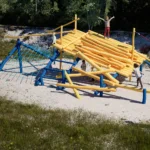 3D-Konzept-Rendering der Spielanlage Isarfloss mit Holzladung auf Fallschutzkies von Wiese umgeben nahe einer ehemaligen Flussböschung